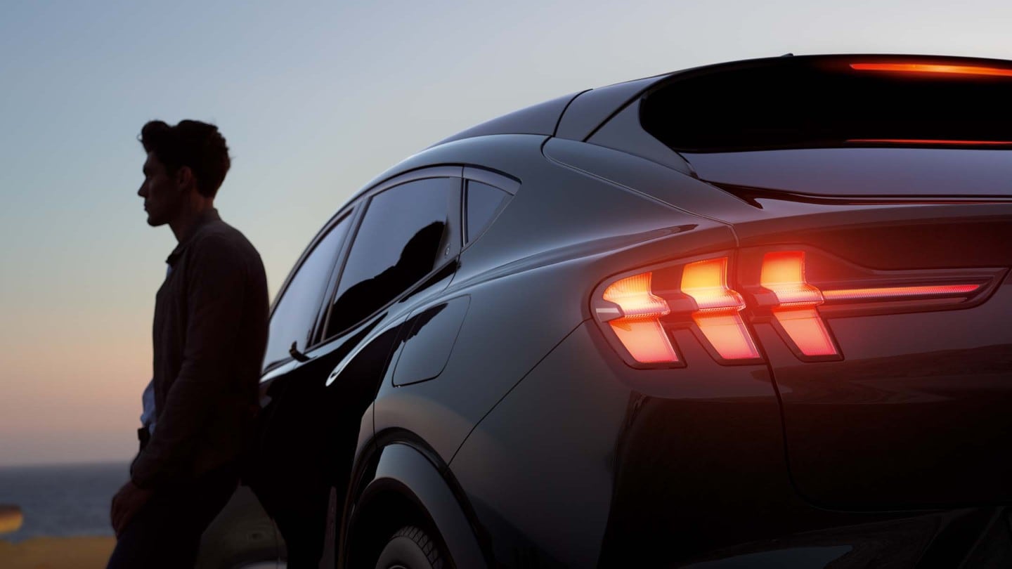 Silhuett av en man och bakdelen av en Mustang Mach-E i solnedgång